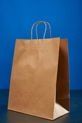 A brown paper bag with handles on a blue background. ECO bag. Craft paper bag. Recycled paper. Environmentally friendly bags.