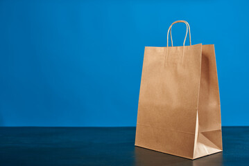 A brown paper bag with handles on a blue background. ECO bag. Craft paper bag. Recycled paper. Environmentally friendly bags.