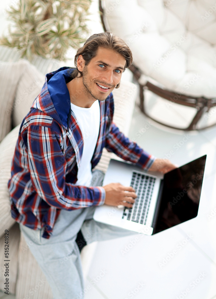 Wall mural young man working on laptop and looking at camera. view from above