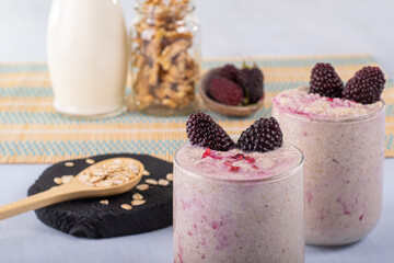 Overnight oat with blackberry fruits, on its right a wooden spoon with oatmeal, and in the...