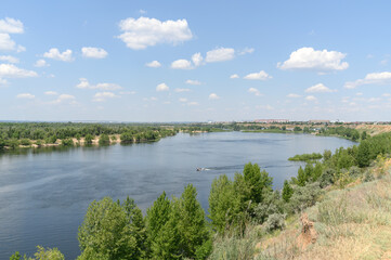 Summer landscape with a river and blue sky during the day. The boat floats on the river.