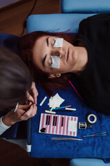 Obraz premium Beautiful young redhead woman at eyelash extension procedure. Cosmetics and body care close up shot. Shallow depth of field and selective focus.