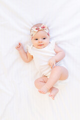 baby girl smiling lying on a white cotton bed at home on her back