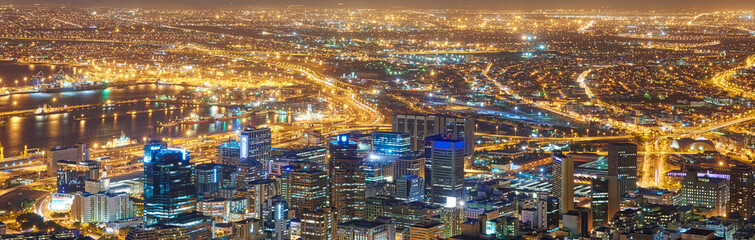 Fototapeta na wymiar Wide angle of a city at night from above. Futuristic panorama of the lights of Cape Town at sunset. .A modern urban landscape of an illuminated city. High angle view from Signal Hill in South Africa