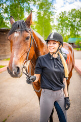 Lovely young woman wearing helmet stroking to her brown horse