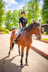Fototapeta premium Lovely young woman wearing helmet riding her brown horse