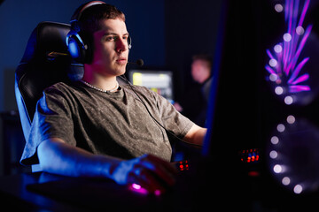 Side view portrait of Caucasian young man playing video games in dark with neon accent lights