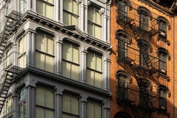 Fototapeta na wymiar Cast iron and brick facades of Soho loft buildings with fire escapes at sunset. Soho Cast Iron Building Historic District, Lower Manhattan, New York City