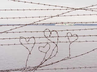 Heart shapes in rusty barbed wire, selective focus with blurry sea and coast in the background....