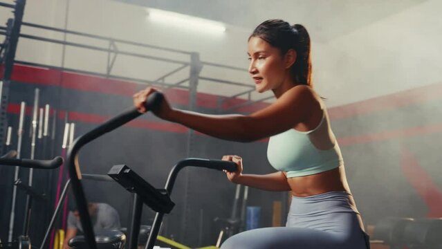 Close up shot of Asian woman exercising on air bike at gym.