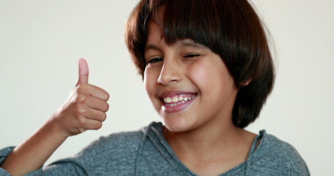 Handsome mixed race child gives thumb up winking to camera. ethnically diverse kid giving approving gesture