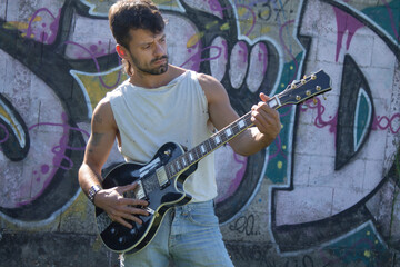 Obraz na płótnie Canvas young man with electric guitar on graffiti wall
