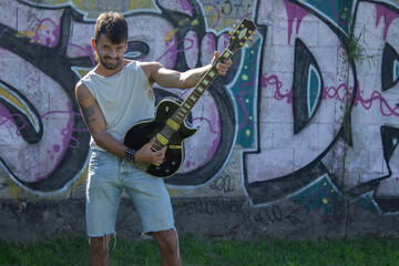 young man with electric guitar on graffiti wall