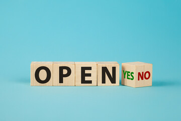 The word OPEN is written on wooden cubes. The hand turns the wooden cube and changes the word NO OPEN to YES OPEN