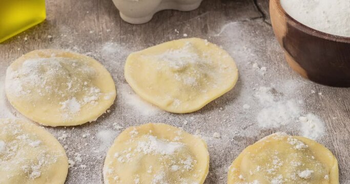 Uncooked stuffed raviolonis or raviolis with flour over wooden table
