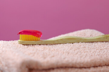 Bamboo Ecological Toothbrush with Red Paste on Towel, pink background, place for text