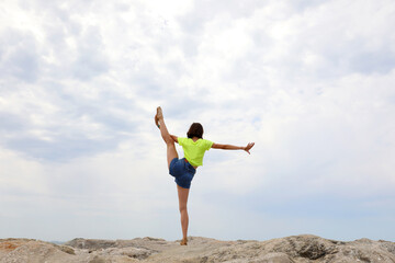 girl does gymnastic exercises to train her balance by stretching herself on a single range on the rocks of the rocks