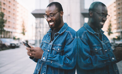 Happy dark skinned tourist in trendy eyewear using cellphone application for checking content...