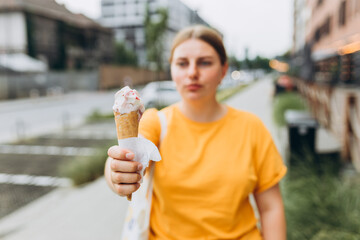 Happy brunete woman eating ice cream in the park, focus on ice cream. Young smiling girl dressed in yellow t-shirt holding ice cream. Food banner