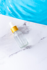 Glass dropper bottle on a marble background near the water, face and skin care products, spa and beauty concept, summer beauty background