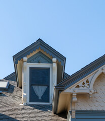 A cupola of a house. The trim is very decorative. The trim is white and the overhang is blue green. There is lace curtain in the window.