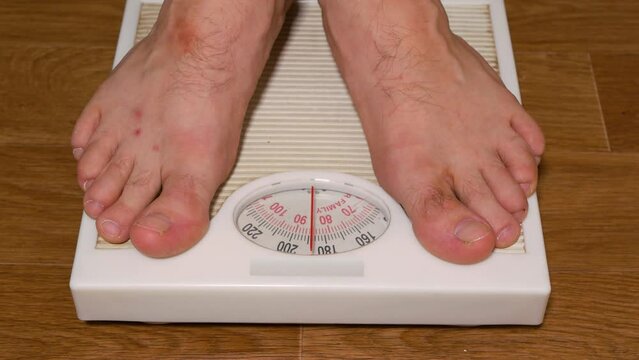 A man weighs himself on a floor scale. A man stands with his bare feet on a white pointer floor scale. Weight control.