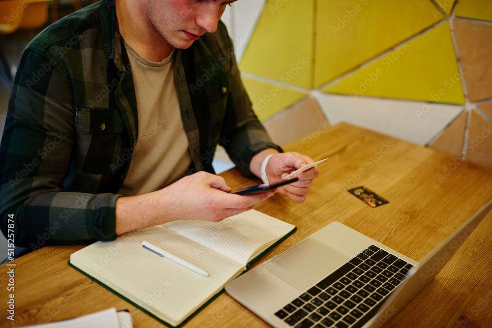 Poster young smiling man texting message on mobile phone while sitting at the desk. using technology. diali