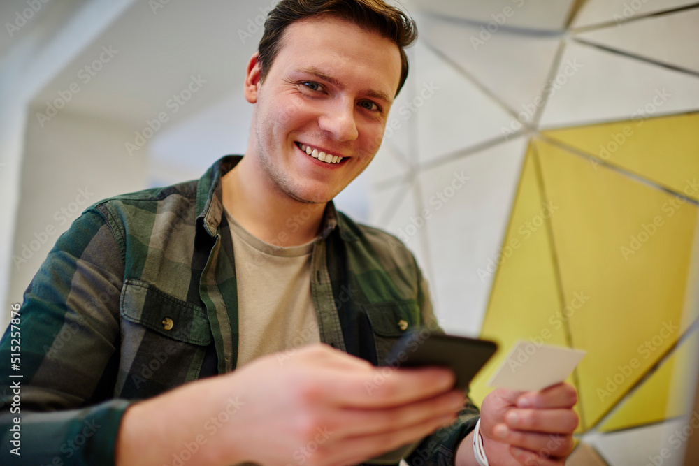 Poster young smiling man texting message on mobile phone while sitting at the desk. using technology. diali