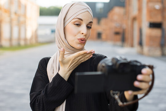 Muslim woman use camera selfie and taking picture in city. Young girl tourist traveler travel alone on street use cell phone record vlog on holiday vacation trip blowing an air kiss to her audience.