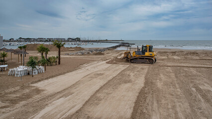 A bulldozer moves sand on a beach to level and maintain it
