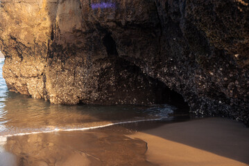 Relaxing view of a small sea wave coming to the limestone rocks on the beach of Noja coastline at sunrise, Cantabria, Spain