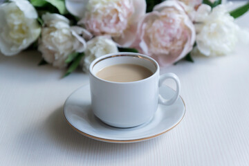 Cup of coffee and white peonies on a wooden background. Top view, copy space.