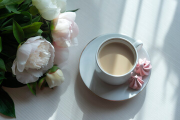 Cup of coffee and white peonies on a wooden background. Top view, copy space.