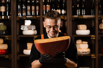 Happy cheese sommelier holding limited gouda cheese and smile. Creative worker of cheese shop....