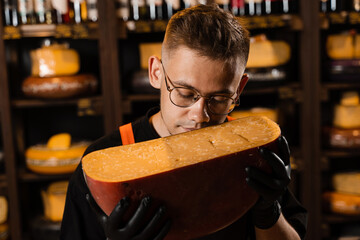 Handsome bearded cheese sommelier in fashion glasses holding and sniff limited gouda cheese. Snack...