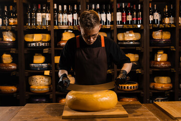 Cheese sommelier cutting yellow cheese wheel cut in half with a knife on the table. Limited maasdam cheese wheel cutting cheese in store.