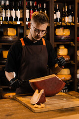 Handsome cheese sommelier with big knife for cut cheese. Bearded hipster in fashion glasses working in cheese shop. Creative idea for advertising.