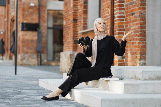 Muslim woman use camera and taking selfie picture. Young girl tourist traveler travel alone on street use camera for record vlog on holiday vacation trip and speaking to her audience sitting on stairs