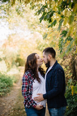 Pregnant young woman stands next to her husband and hugs him in the countryside in the fall. The future father gently touches the belly of the expectant mother. High quality photo.