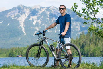 The guy sits on the grass near the bike against the background of the mountains.