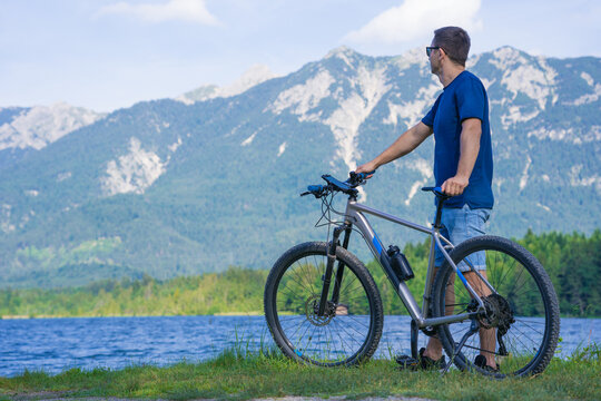 The guy sits on the grass near the bike against the background of the mountains.