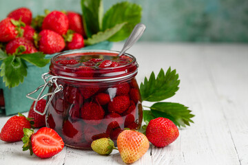 Strawberry jam with whole berries on a white wooden table. Selective focus