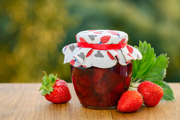 Strawberry jam with whole berries on a wooden table in the garden. Selective focus