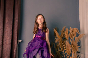 Obraz premium Portrait of a teenage girl in a purple dress in a room. The girl on the background of a gray wall.