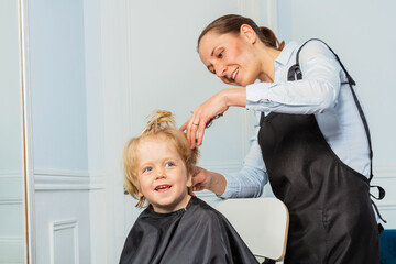 Smiling boy get haircut at barbershop by professional stylist