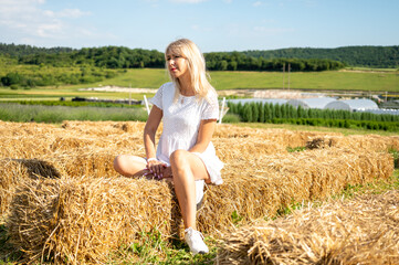 Naklejka na ściany i meble young fair-haired girl sitting on hay, freshly cut haystacks, straw, looking to the side 