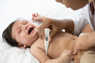 doctor measuring baby's temperature and baby crying on bedroom
