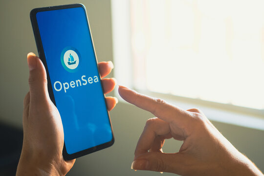 June 26, 2022, Brazil. In this photo illustration, a woman's holds a smartphone with the OpenSea logo displayed on the screen.