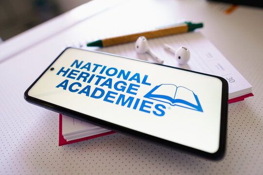 June 30, 2022, Brazil. In this photo illustration the National Heritage Academies logo seen displayed on a smartphone next to a book with pen and headphones.