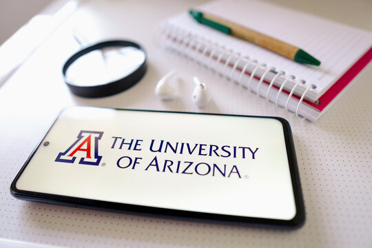 June 30, 2022, Brazil. In this photo illustration the University of Arizona logo seen displayed on a smartphone next to a book with pen, headphones and a magnifying glass.